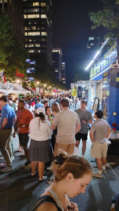crowds walking down a pedestrianized street with vendor stalls selling food and drinks