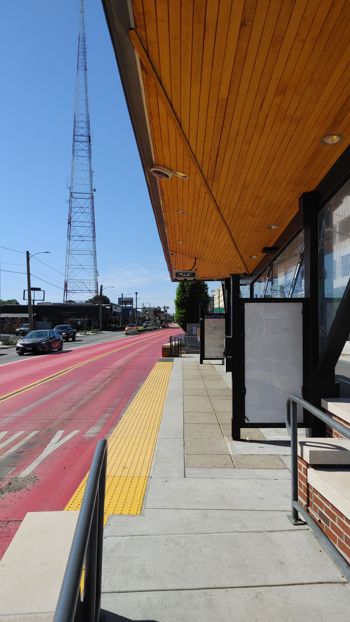photo of BRT stop in the middle of the road. Red bus lanes are on the side and a nice sun covering with wooden panels and lights on the bottom. It's elevated off the ground for platform level boarding