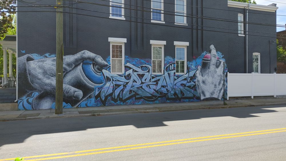 street art featuring hands holding a spray paint can like it's painting existing graffiti