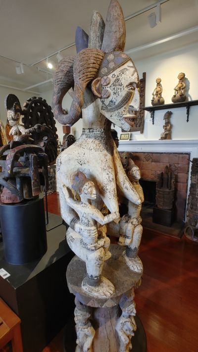 photo of an African statue. It features a mother with long breasts supporting two children. The long breasts were an indication that she had raised surviving children and was a mark of honor.